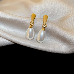 Macro shot of elegant teardrop pearl earrings with golden metallic studs on silk fabric