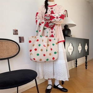 Close-up of white plush tote bag with red and green polka dots held by a model