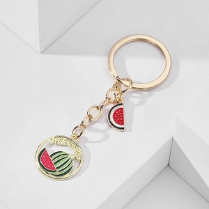 Macro detail of golden alloy keychain featuring a watermelon charm and engraved round pendant