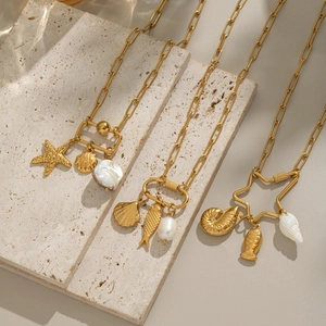 Detailed shot of gold seashell necklaces with baroque pearls and starfish on travertine