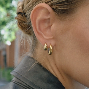 Gros plan d'élégantes boucles d'oreilles créoles C dorées portées par un mannequin