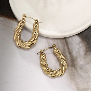 Macro shot of gold-plated twisted U-shape hoop earrings with woven texture on marble
