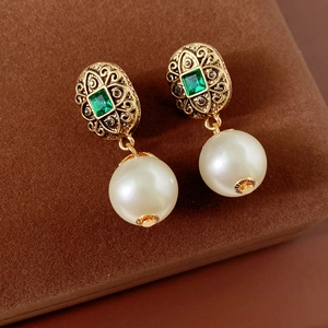 Dettaglio di orecchini vintage con pietre verde smeraldo e grandi perle bianche lucide