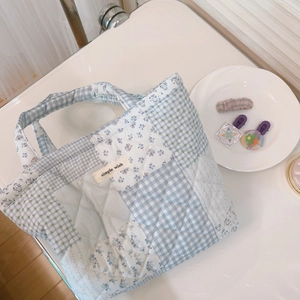 Detail of blue quilted handbag with floral patterns and a simple wish label