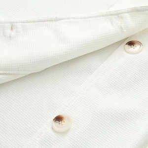 Detail of white waffle texture fabric and amber faux horn buttons on a stylish coat