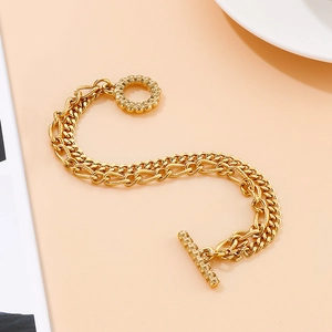 Detailed close-up of double-strand gold chain bracelet with OT toggle clasp on pink background
