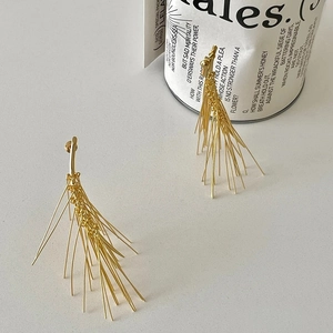 Dettaglio di orecchini minimalisti color oro a forma di aghi di pino con nappe