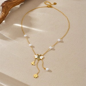 Detail of gold bee pendant necklace with pearls and flowers on a textured background
