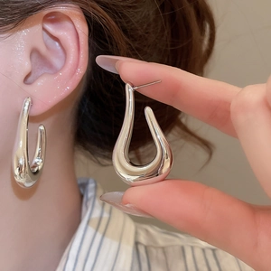 Close-up of teardrop-shaped silver metallic earrings with liquid-like smooth finish