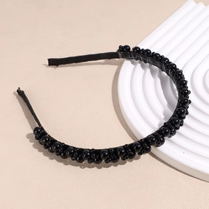 Detail view of a black beaded headband with woven glossy pearls on a white display stand