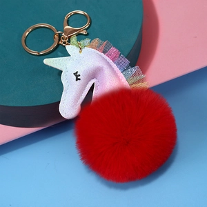 Llavero de unicornio con pompón rojo y tul arcoíris sobre un soporte moderno