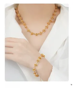Close-up of polished gold-tone knot chain necklace and bracelet set on a white shirt