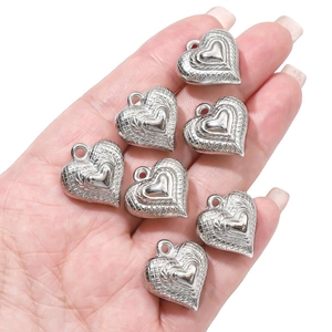 Macro detail of hand-held silver heart pendants with three-layer floral relief patterns