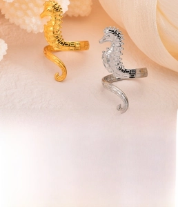Detailed view of seahorse-shaped ring in gold and silver finish on a coral background