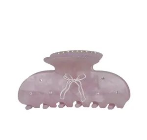 Close-up of a pink acetate hair claw clip with white bow pattern and inlaid rhinestones