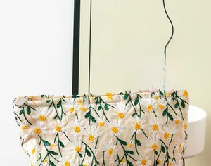 Close-up of embroidered daisy flowers on white canvas cosmetic bag with metal zipper
