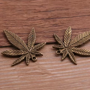 Bronze alloy maple leaf charms with detailed vein textures on a natural wooden background