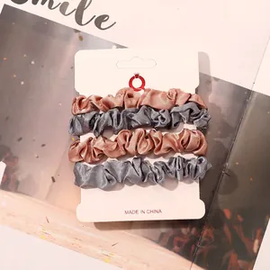Close-up of four satin scrunchies in gold and silver on a white display card