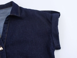 Detail eines dunkelblauen Jeanshemdes mit Umlegekragen und goldener Knopf-Nahaufnahme