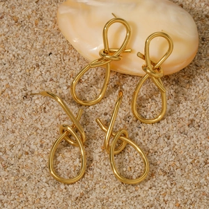 Minimalist gold knotted rope earrings set on a beige textured shell display background