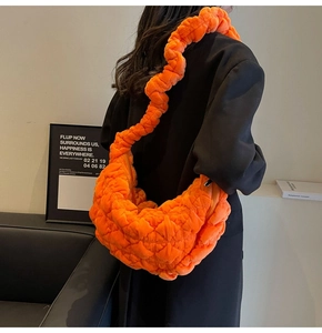 Detail view of orange quilted velvet cloud bag with pleated strap worn by a model