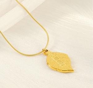 Macro detail of leaf pendant necklace with lucky engraving in gold plated finish