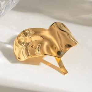 Close-up of golden polished ponytail cuff with elegant hammered wavy texture on white base