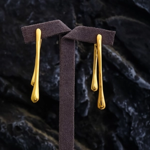 Macro view of gold-plated fluid drop earrings on a dark display stand with mirror finish