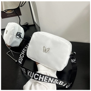 Detail of white nylon crossbody bag with silver butterfly emblem and lettered strap