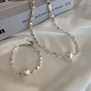 Detail of irregular silver beads and large white pearl necklace on white silk fabric