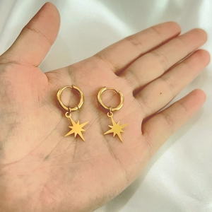 Detail of 18K gold-plated stainless steel hoop earrings with star pendants held in hand