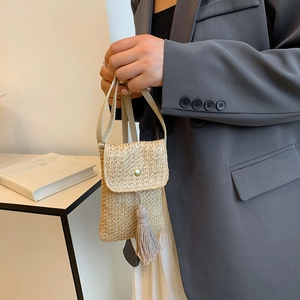 Minimalist straw woven crossbody bag with tassel and gold clasp shown on model