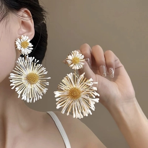 Close-up of white daisy flower earrings with gold center worn by a female model