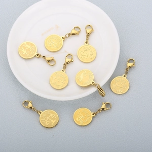 Golden stainless steel zodiac charms with lobster clasps on white ceramic dish