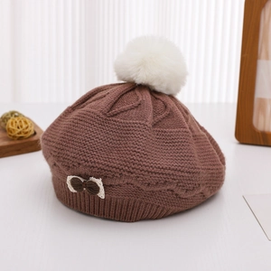 Detailed knit texture of a brown beret featuring a soft white faux fur pompom and lace bow