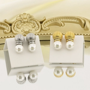 Detailed view of silver and gold pearl stud earrings with rhinestones on a white stand