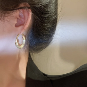 Close-up of golden hollow hoop earring with woven texture shown on a female model
