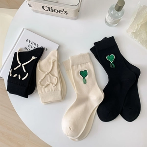 Set di quattro calzini in cotone a metà polpaccio con motivi a cuore e nappine su tavolo bianco