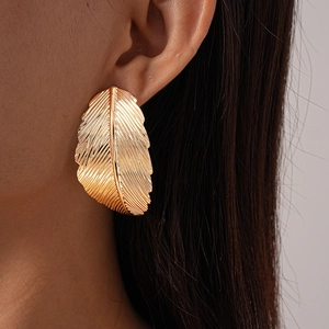 Detailed macro view of large golden feather earrings with intricate carved metallic textures