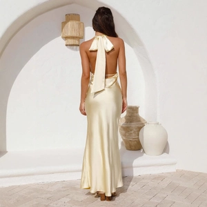 Robe longue dos nu en satin jaune à col licou pour femme dans un décor côtier minimaliste
