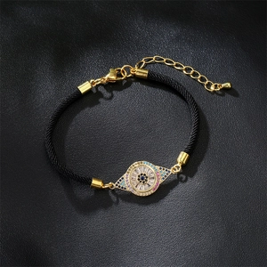 Detailed shot of golden evil eye charm with colorful zircons on black braided cord