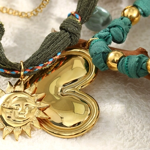 Detailed macro view of 18K gold-plated sun and heart charms on a green woven fabric cord