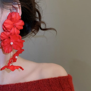 Detail of red fabric flower earrings with pearls and gold chains on a model