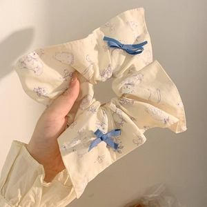 French style beige scrunchie with purple patterns and blue bows held by a hand