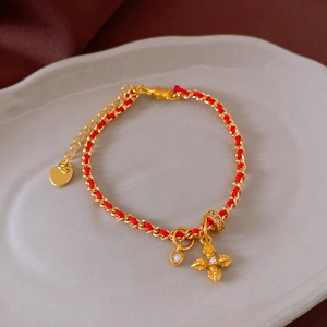 Detail of gold-plated bracelet with red cord, zircon heart and cross pendant on plate