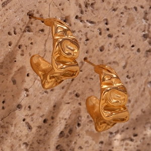 Macro shot of gold earrings with irregular lava texture on a rustic beige stone