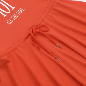 Detail of orange dress fabric showing white letter print and drawstring with metal tip