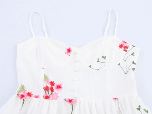 Détail d'une robe blanche à bretelles avec broderie florale et boutons en perles au buste
