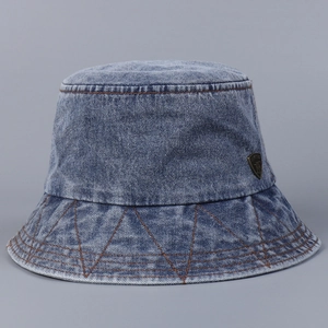 Detail of washed denim bucket hat with contrast stitching and metal shield emblem