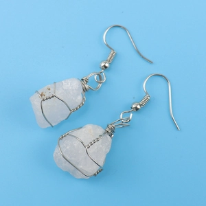 Detail of silver wire-wrapped raw white crystal earrings on a blue background